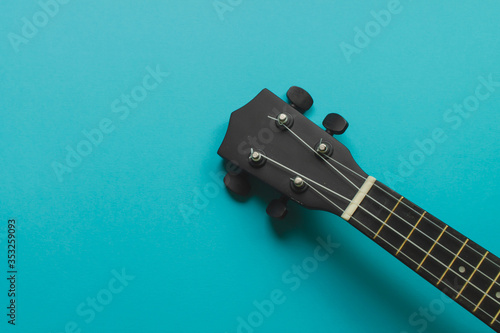 Body of a bright black ukulele guitar against a bright blue back photo