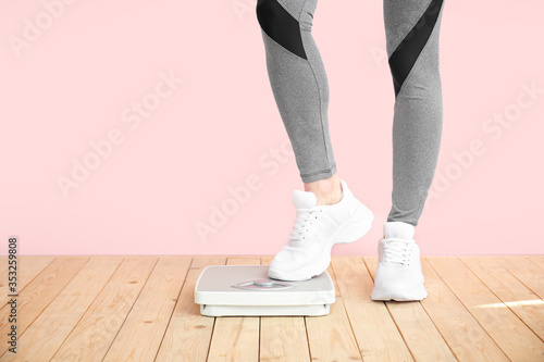 Young woman measuring her weight near color wall