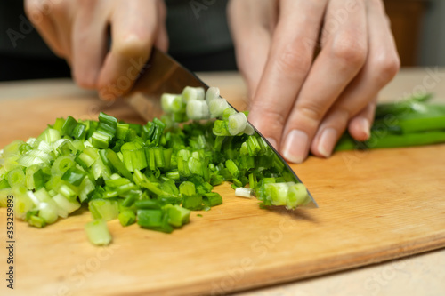 Women's hands cut green onions with a knife on a wooden Board close up