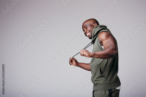 African American man in a tracksuit holds a rope hood from a hood with his hands and smiles happily in a studio photo