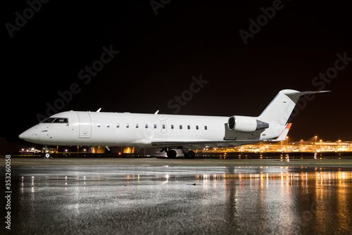 A white business Jet parked at night on a wet apron producing nice reflections