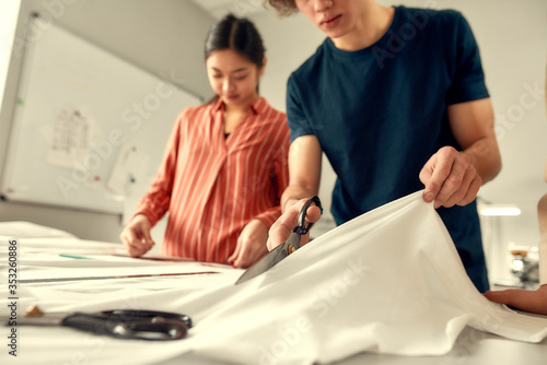 Out of the best materials. Cropped shot of young male designer cutting white fabric textile in a studio. Group of creative millennials working together photo