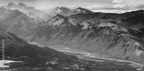 fotografía panorámica en blanco y negro. Río rodeado por grandes montañas y nubes 