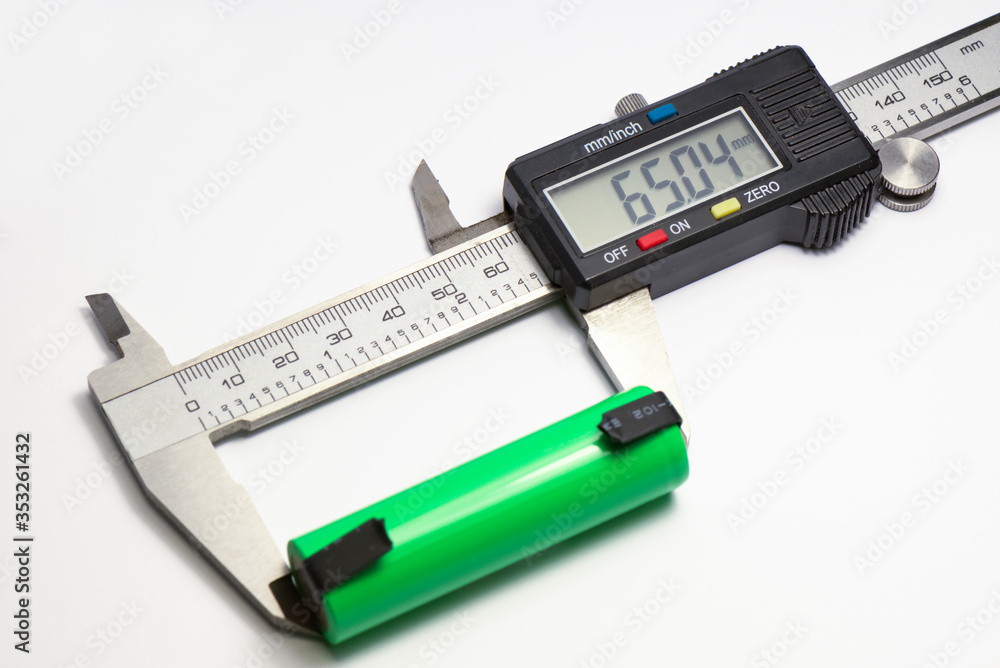 Measuring the length of a new green rechargeable lithium ion battery with an electronic caliper. Measurement value on the display. Measuring the length of a new green rechargeable lithium ion battery with an electronic caliper. Measurement value on the display.