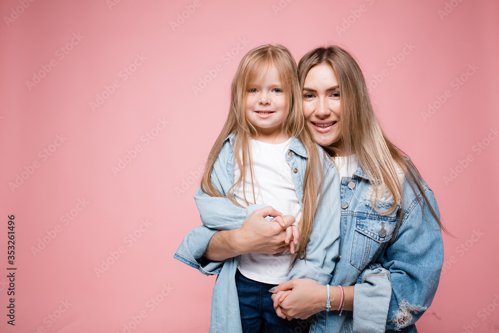 Long-haired mom and daughter hugging each other tightly on a pink background. Happy parent-child relationship Long-haired mom and daughter hugging each other tightly on a pink background. Happy parent-child relationship