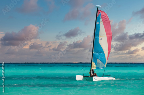 A man sails near the beach in a Hobie-Cat in the turquoise waters of the Mexican Caribbean at sunset.