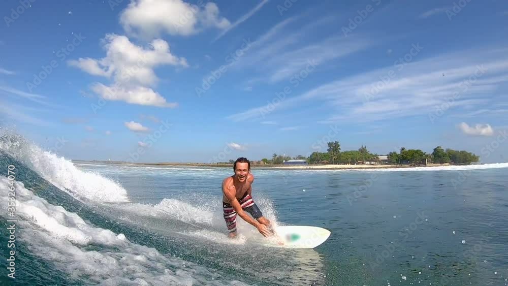 SLOW MOTION, PORTRAIT: Cheerful Caucasian surfer gives the shaka while riding a fun wave. Stoked male tourist on vacation in the Maldives surfs on a sunny summer day. Surfer riding glassy waves. SLOW MOTION, PORTRAIT: Cheerful Caucasian surfer gives the shaka while riding a fun wave. Stoked male tourist on vacation in the Maldives surfs on a sunny summer day. Surfer riding glassy waves.