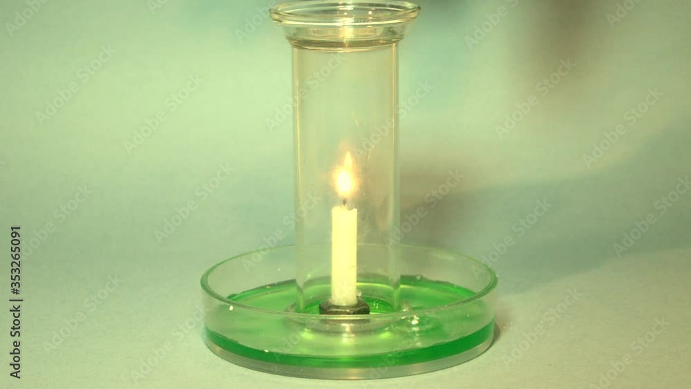 A glass is placed over a burning candle that stands in water (green for