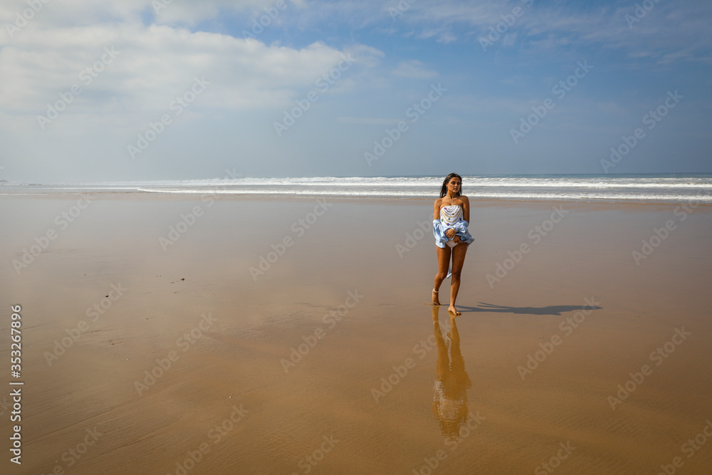 The Atlantic Ocean. Beautiful young girl in a white swimsuit and blue shirt on the ocean.