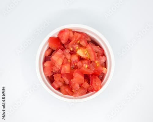 Chopped red tomato in a white porcelain bowl over white background