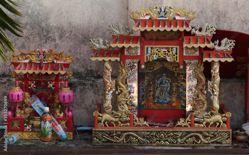 chinese mini shrine located on the ground on a temple wall with grocery goods as donations for buddha