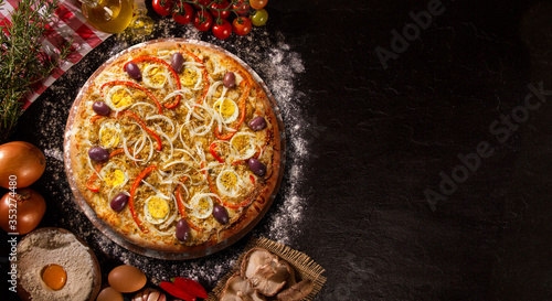 Tasty portuguese pizza and cooking ingredients tomatoes basil on black concrete background. Top view.