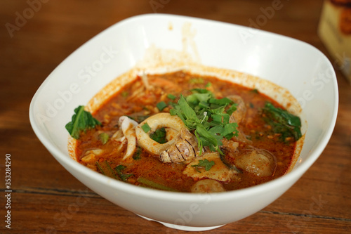 Spicy seafood tum yum noodle soup in white bowl on timber table