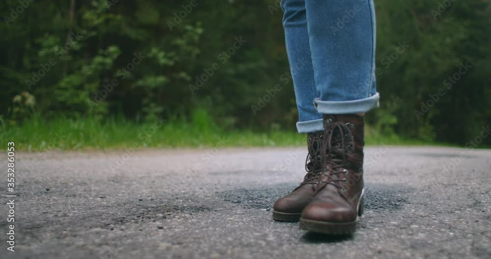 Close-up of feet in boots in slow motion walking on an asphalt road. Hitchhiking. Female traveler Close-up of feet in boots in slow motion walking on an asphalt road. Hitchhiking. Female traveler