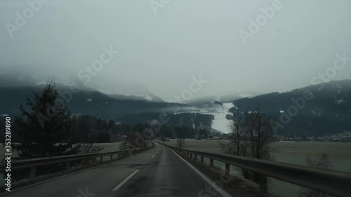 Driving on a gloomy dark road near mountains partially covered in snow photo