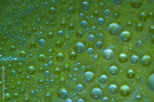 Abstract green background of drops and droplets. Close up. Illuminated by the bright sun malachite-green drops of water are located on a green glass surface. 