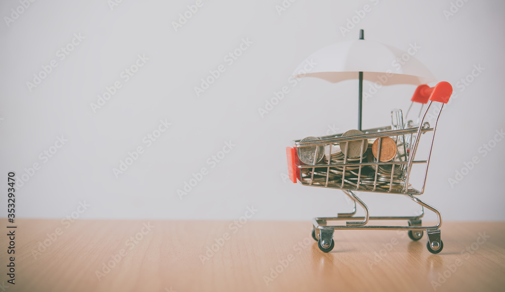 Umbrella is on the currency, the coin is in a shopping cart that is placed on the wooden floor. The concept of protection and protection and safety supervision in business Umbrella is on the currency, the coin is in a shopping cart that is placed on the wooden floor. The concept of protection and protection and safety supervision in business