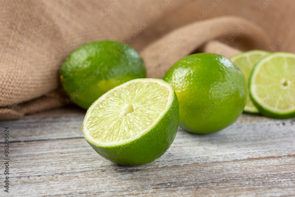 A view of several green limes, featuring on in the center that is cut open showing the segment texture, in a still life setting. A view of several green limes, featuring on in the center that is cut open showing the segment texture, in a still life setting.