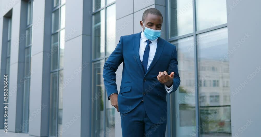 African American young businessman inmedical mask, suit and tie spraying disinfector on hands and cleaning them from germs at street. Man during coronavirus pandemic disinfecting skin. Clean and safe. African American young businessman inmedical mask, suit and tie spraying disinfector on hands and cleaning them from germs at street. Man during coronavirus pandemic disinfecting skin. Clean and safe.