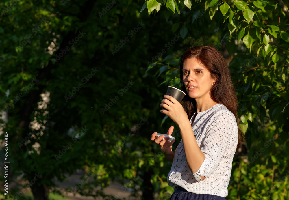 Smiling woman with dark hair holding coffee cup in a garden