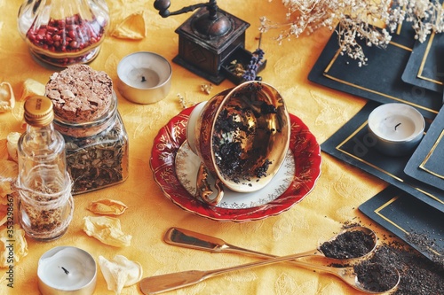Vintage teacup laying on it's side on a wiccan witch altar for reading tea leaves as a method of divination to foretell the future. Bright yellow cloth in photo with nature elements and tarot cards photo