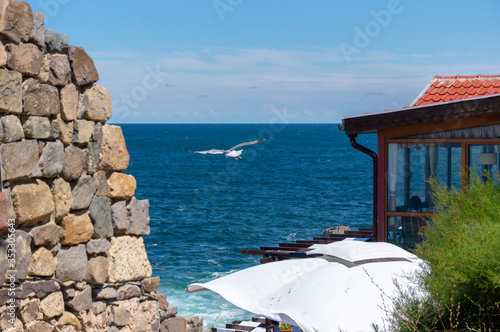 Fragment of the fortress wall  white umbrella and restaurant terrace by the sea