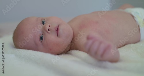 Funny portrait of newborn baby lying on bed and looking surprisely aside photo