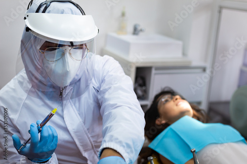 Dentist preparing anesthesia srynge to apply to young female patient photo