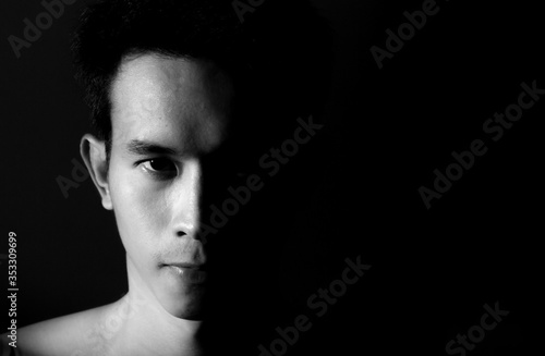 Straight on black and white head shot of a man looking into camera with half his face shadowed on a black background