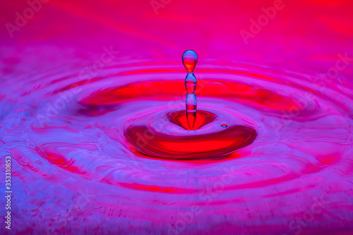 splash of a drop of water on a color gradient burgundy violet surface close-up