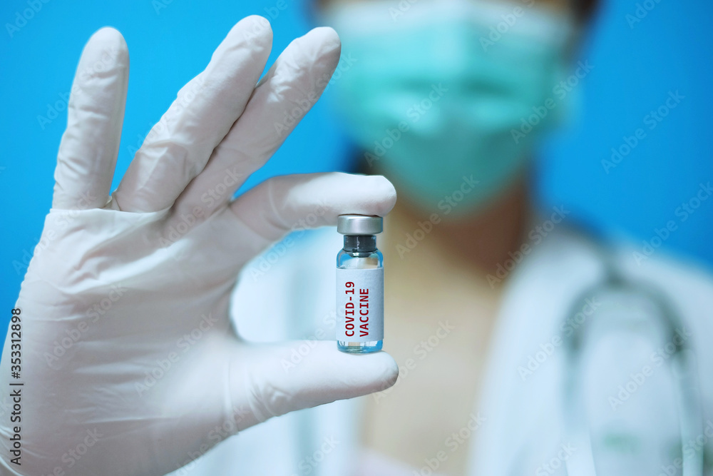 A female Asian physician with surgical mask and white rubber gloves at a clinic, holding a glass bottle of 1 dose covid-19 vaccine, with white background and red letters. A female Asian physician with surgical mask and white rubber gloves at a clinic, holding a glass bottle of 1 dose covid-19 vaccine, with white background and red letters.