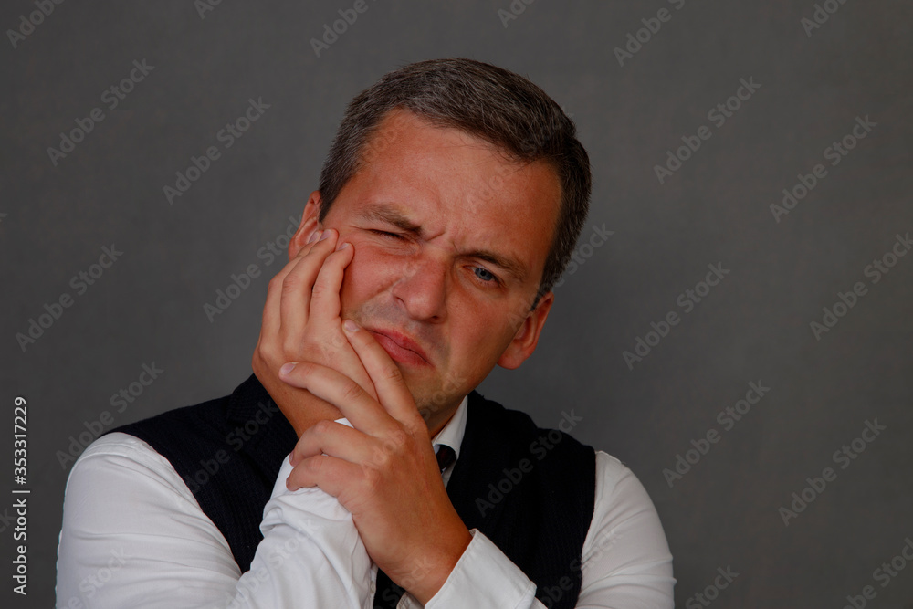 A man holds his cheek from a toothache. A man grabs a toothache from his face. Portrait of a man against toothache closeup on a gray background. A man holds his cheek from a toothache. A man grabs a toothache from his face. Portrait of a man against toothache closeup on a gray background.