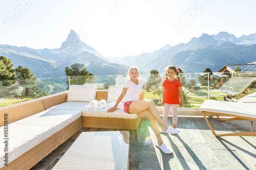 Mom with daughter relaxing in the rustic wooden terrace on mountain, alpine view