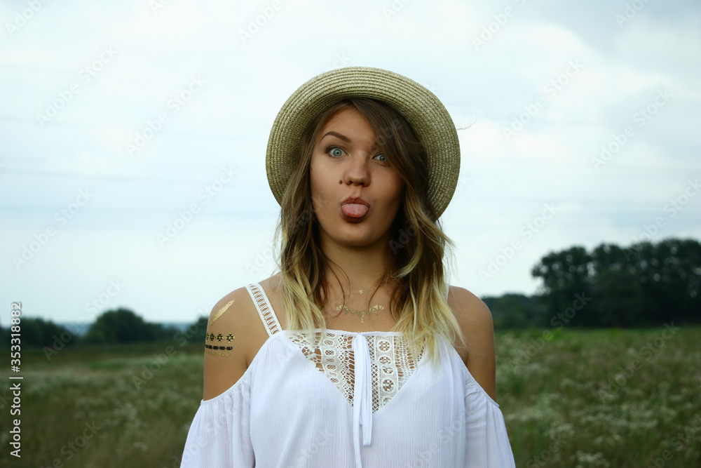 portrait of a happy flirty beautiful woman in white blouse and straw hat in the field. Temporary tattoo. Drawings on body. hippie. Nature loving.