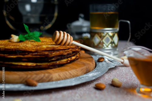 a spoon for honey lies on pancakes. pancakes stacked on a wooden board. pancakes with tea
