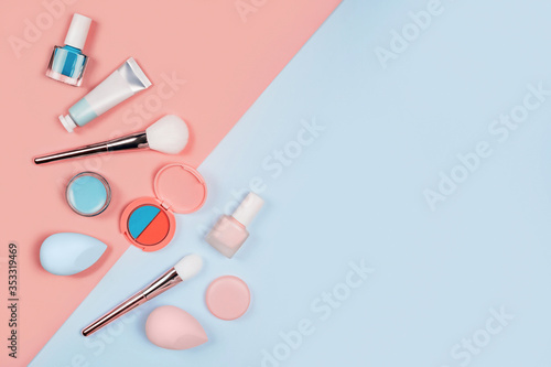 Makeup products with brushes, nail polish, sponges, eyeshadow, cream and lipstick on coral-blue color background. Flat lay, top view, space for text.