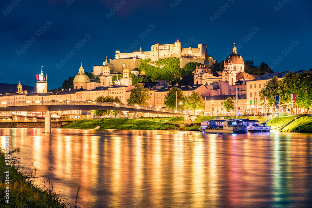 Naklejka premium Stare miasto Salzburga odbija się w spokojnych wodach rzeki Salzach. Spektakularny nocny pejzaż Salzburga z zamkiem Hohensalzburg w tle. Austria, Europa. Podróżowanie koncepcja tło.