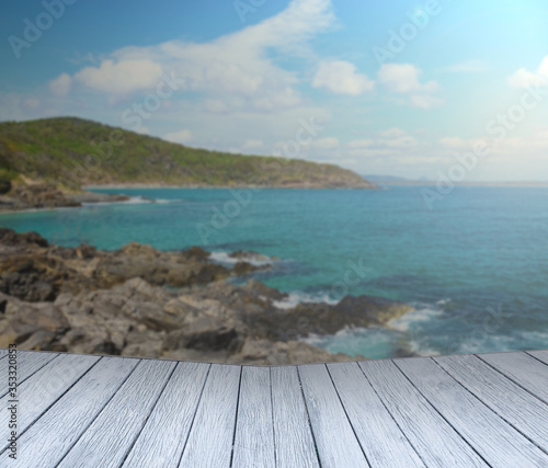 Empty wooden bridge or table top with blurred ocean with rock and mountain background. Morning light.