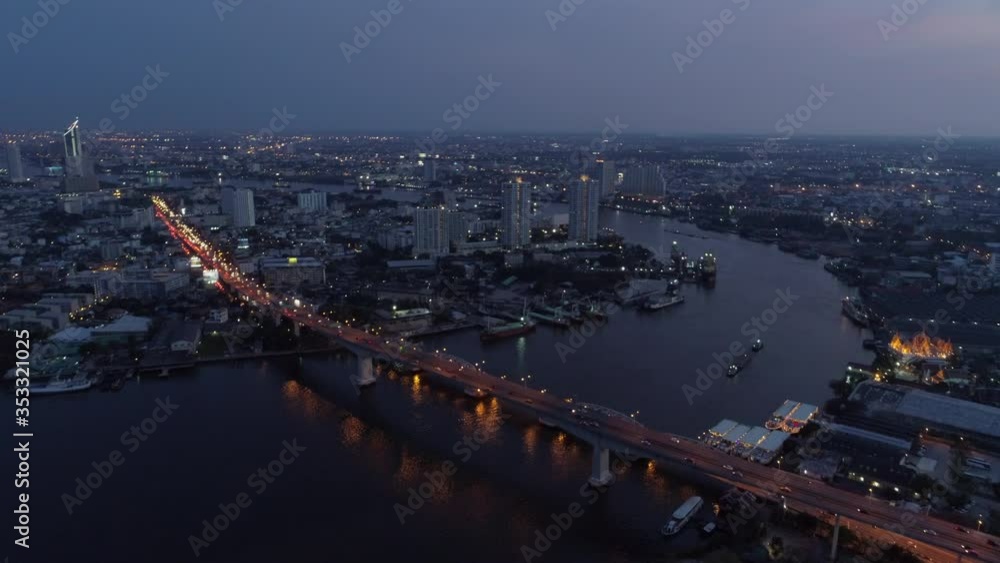 Aerial shot of vehicles on illuminated bridge over river in city at dusk, drone flying forward over cityscape against sky - Bangkok, Thailand Aerial shot of vehicles on illuminated bridge over river in city at dusk, drone flying forward over cityscape against sky - Bangkok, Thailand