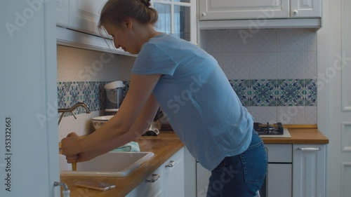 Young woman cleaning a blockage in a kitchen sink with a plunger in her hands. Plumbing in need of repair. Housekeeping