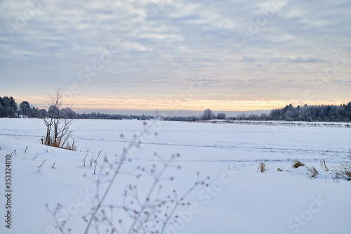 View from the shore of a river or lake, when the water is covered with ice powdered with snow. Morning or evening winter landscape © keleny