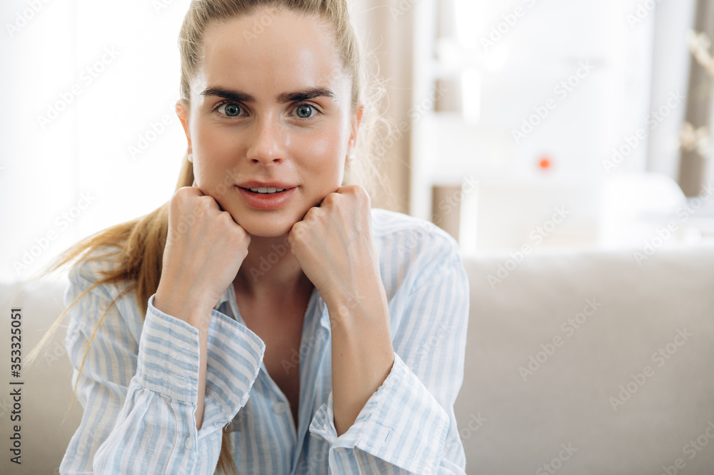 Close-up female portrait. Confident beautiful blue-eyed сaucasian girl in home clothes in a positive mood sitting at home on the couch Close-up female portrait. Confident beautiful blue-eyed сaucasian girl in home clothes in a positive mood sitting at home on the couch