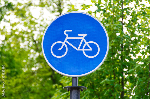Sustainable transport. Blue road sign or signal of bicycle lane with green trees and nature background