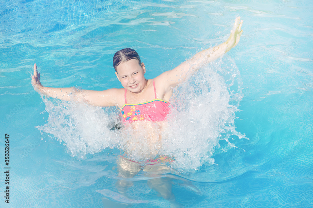 naughty game with water in an outdoor pool at a summer resort. a happy girl in a bright swimsuit jumps in the water with splashes from her hands. Summer vacation and healthy lifestyle concept