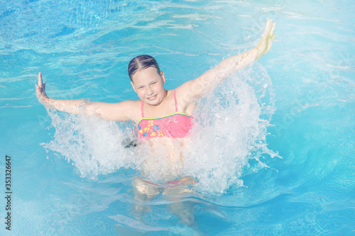 naughty game with water in an outdoor pool at a summer resort. a happy girl in a bright swimsuit jumps in the water with splashes from her hands. Summer vacation and healthy lifestyle concept