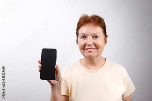 Senior woman shows a phone on a white background in a light T-shirt. place for text, isolated