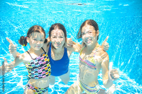 Family swims in pool under water, happy active mother and children have fun, fitness and sport with kids on summer vacation 