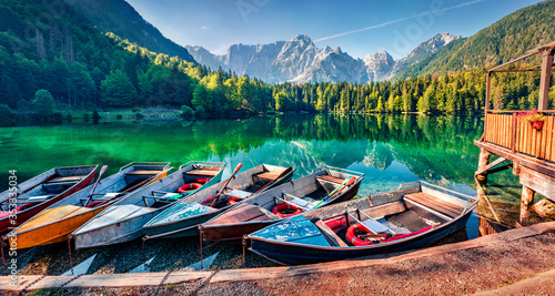 Six pleasure boats on Fusine lake. Calm morning view of Julian Alps with Mangart peak on background, Province of Udine, Italy, Europe. Traveling concept background.