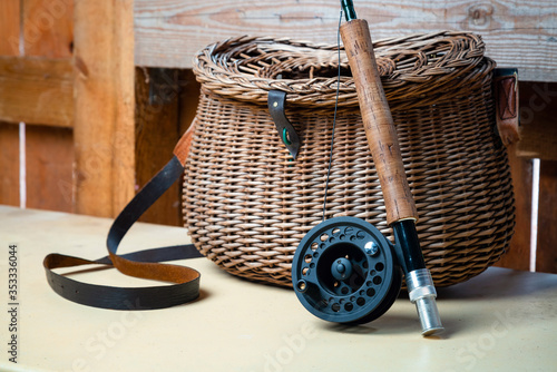 Close up of fly fishing rod with reel next to braided basket. Fly fishing equipment still life. Nobody