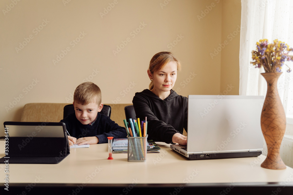 Mother using laptop and tablet teaching with her son online at home in his room